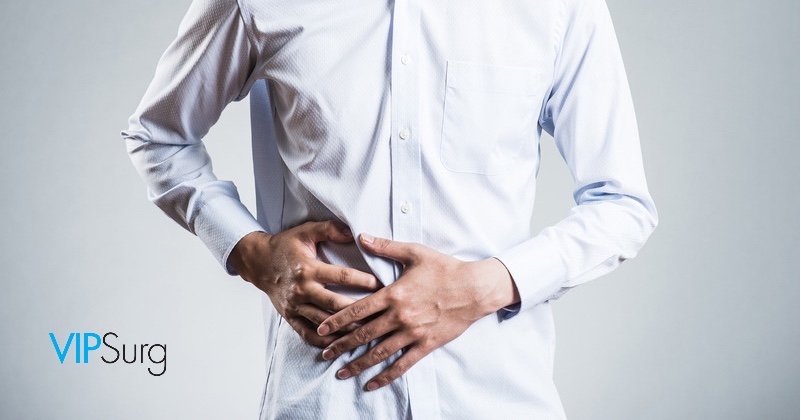 Man in dress shirt holds hands on lower abdomen to relieve abdominal pain he has been avoiding treatment for. Strive Surgery  Las Vegas logo at bottoms left corner. 