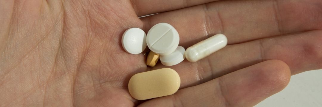 Hand holding multiple pills of varying shapes and sizes