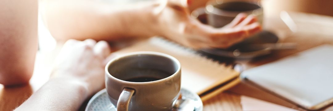 Two people at coffee shop table talking with cups of coffee on table 
