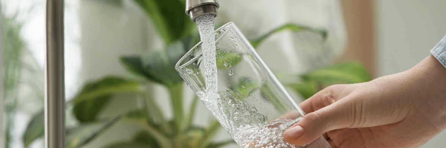 Woman pouring water into glass from sink tap 