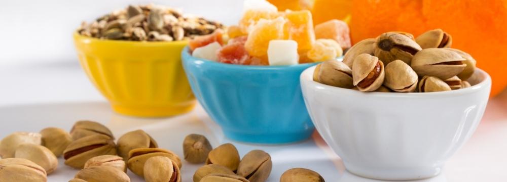 three bowls with different snacks, left bowl contains seeds, middle bowl contains fruits, right bowl contains nuts